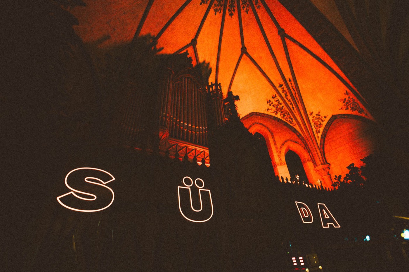 SÜDA in neon under the vaulted ceiling and organ of a church